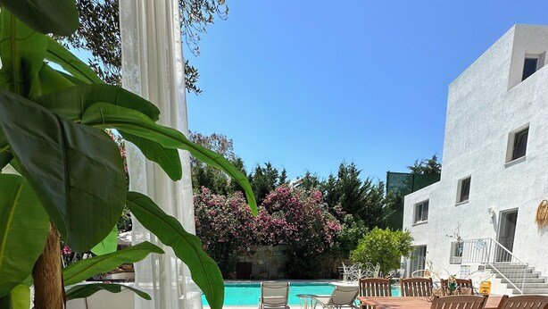 A poolside area with a wooden deck, lounge chairs, and a white building in the background. - Mumu Bodrum Hotel (Bodrum)
