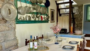 A dining area with a table set for two, a wall-mounted pot rack, and a stone wall. - House on hillside with garden. Relaxation near Lucca and the sea. Pets allowed (Fibbiano)