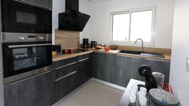 A modern kitchen with a built-in oven, a coffee maker, and a sink. - Gîte L'angélique - Fleurs des Pyrénées - Vue Hautacam (Argelès-Gazost)