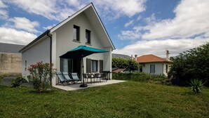 A modern two-story house with a covered patio area featuring outdoor furniture. - Gîte L'angélique - Fleurs des Pyrénées - Vue Hautacam (Argelès-Gazost)