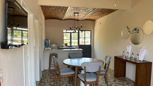 Ein Essbereich mit rundem Tisch und vier Stühlen, ein Küchenbereich mit einer Theke und Spüle sowie eine Decke mit sichtbaren Holzbalken.