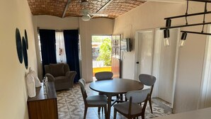 Ein kompakter Wohnraum mit einem runden Esstisch, zwei Stühlen, einer Couch, einem Schrank und einem Deckenventilator.