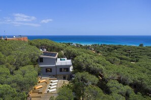 Ein modernes Haus mit Dachterrasse, umgeben von üppiger Vegetation und Blick auf das Meer.