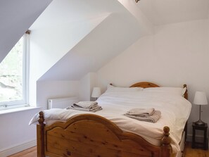 A bedroom with a sloped ceiling, a wooden bed frame, white linens, and a bedside table with a lamp.