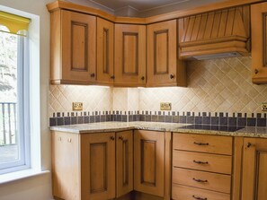 Een keuken met houten kastjes, een betegelde spatwand en een raam met een geel blind.