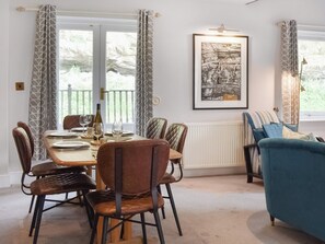 Un coin repas avec une table dressée pour quatre personnes, entourée de six chaises. Une œuvre d’art en noir et blanc représentant un paysage urbain, encadrée, est accrochée au mur.