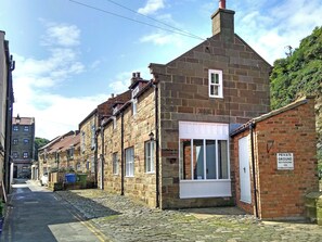 Une ruelle étroite pavée, bordée de bâtiments en pierre, avec une plaque d’identification privée et une porte blanche.
