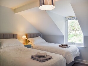 Une chambre avec deux lits, une table de chevet, une lampe et une fenêtre donnant sur un paysage verdoyant.