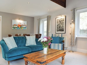 Een woonkamer met een blauwgroene bank, een houten salontafel, en een eethoek met stoelen en een tafel.