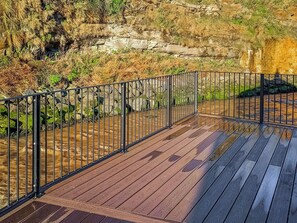 Une terrasse en bois avec une rambarde en métal, donnant sur une falaise rocheuse et une rivière.