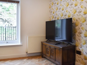 Una habitación con una televisión sobre un mueble de madera, una ventana con vistas a zonas verdes y papel tapiz con motivos florales.