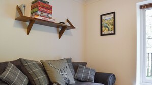 Een woonkamer met een grijze bank, geruite kussens, een houten plank met gezelschapsspellen en een lijst met een afbeelding van St. Aethan's.