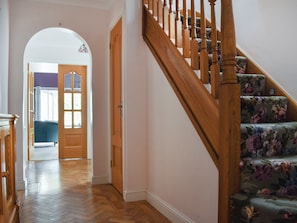 Un pasillo con una escalera de madera que conduce a una habitación con alfombra floral.