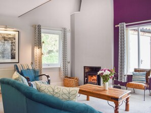 Un salon comprenant un canapé, une table basse en bois, une cheminée et une vue sur l’extérieur grâce à de grandes fenêtres.