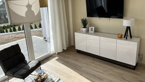Uma sala de estar moderna com um sofá, uma mesa de centro de vidro, uma televisão e um armário branco.