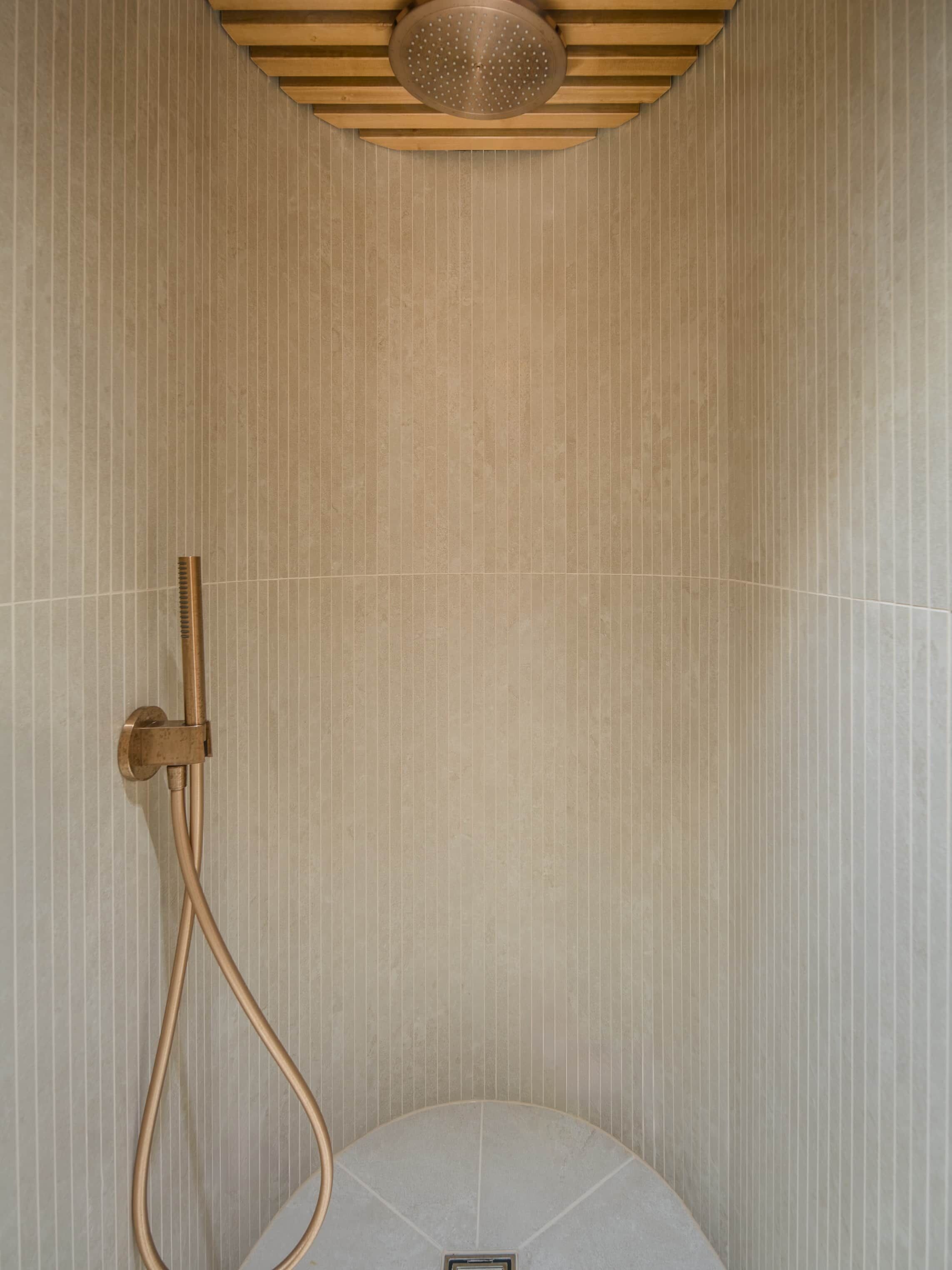 A shower with a curved design, a handheld showerhead, and a wall-mounted control.