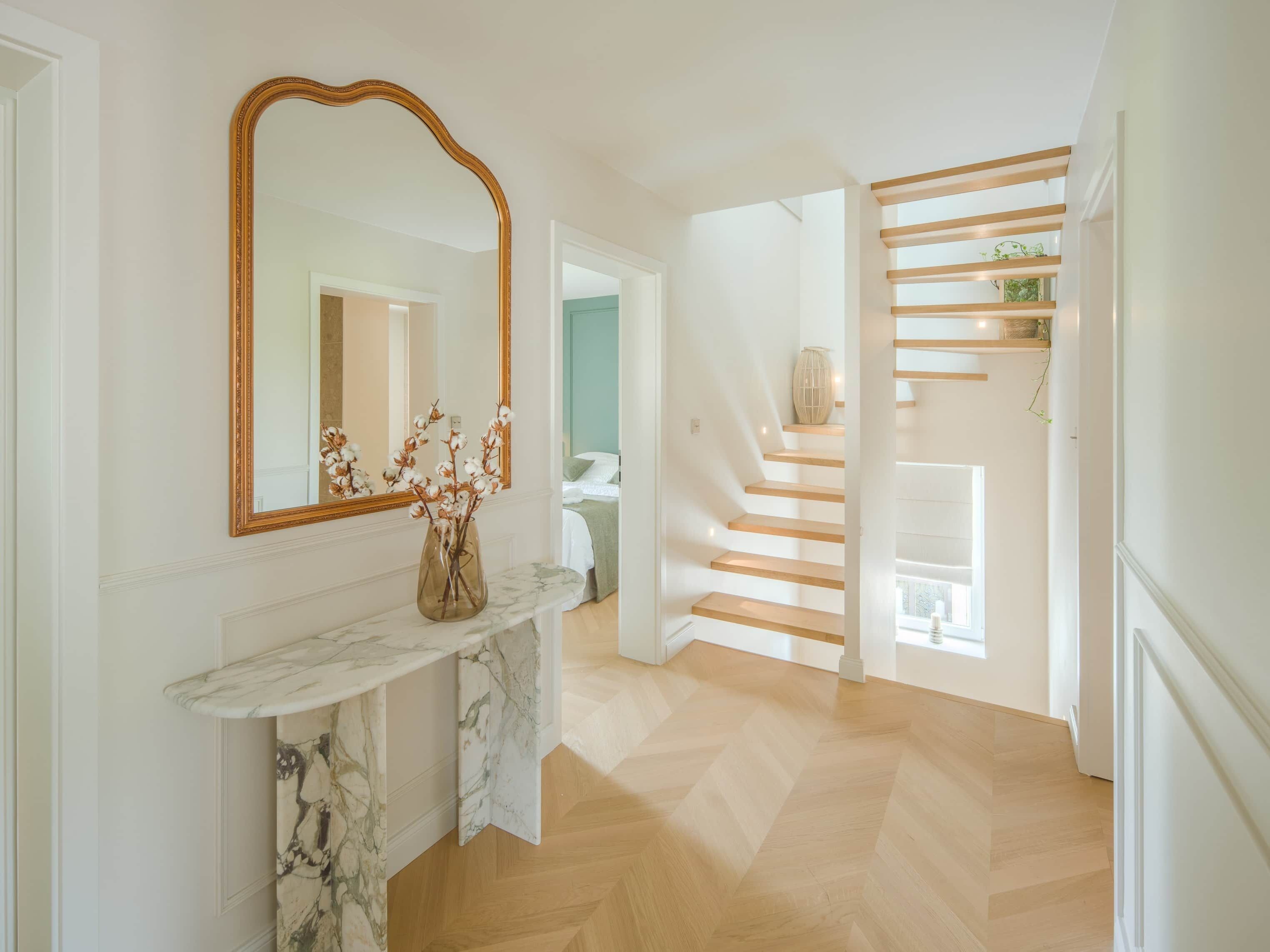 A hallway with a marble console table, a large mirror, and a staircase with wooden steps.