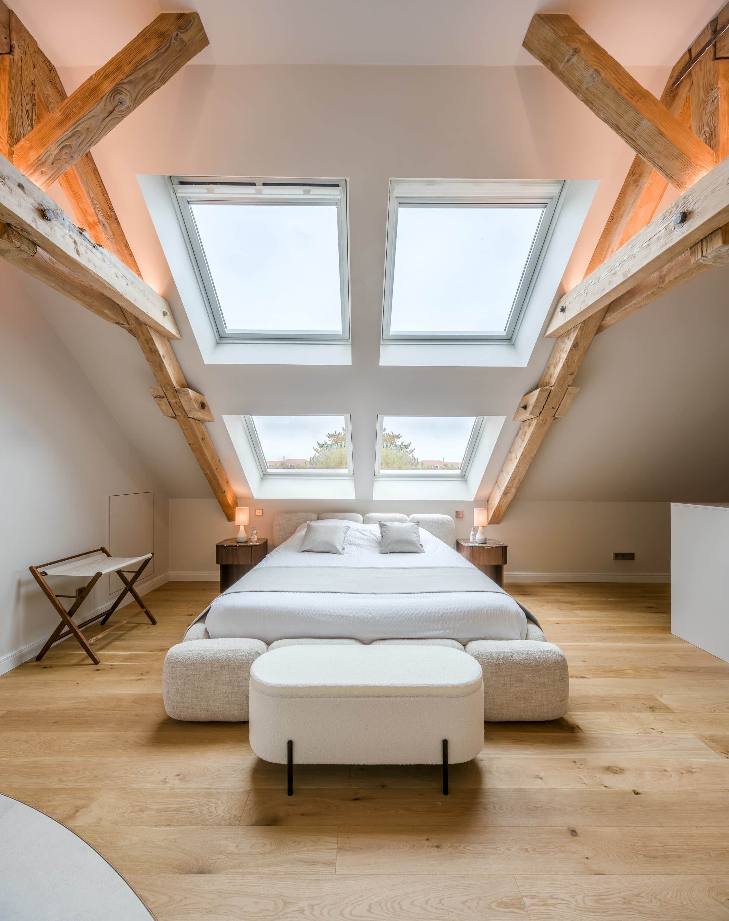 Ein Schlafzimmer mit einer Lofts-Decke, zwei Dachfenstern, einem Bett mit weißer Bettwäsche und einer Bank.