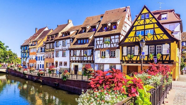 A row of traditional half-timbered houses along a canal with a bridge and flower-lined walkway.
