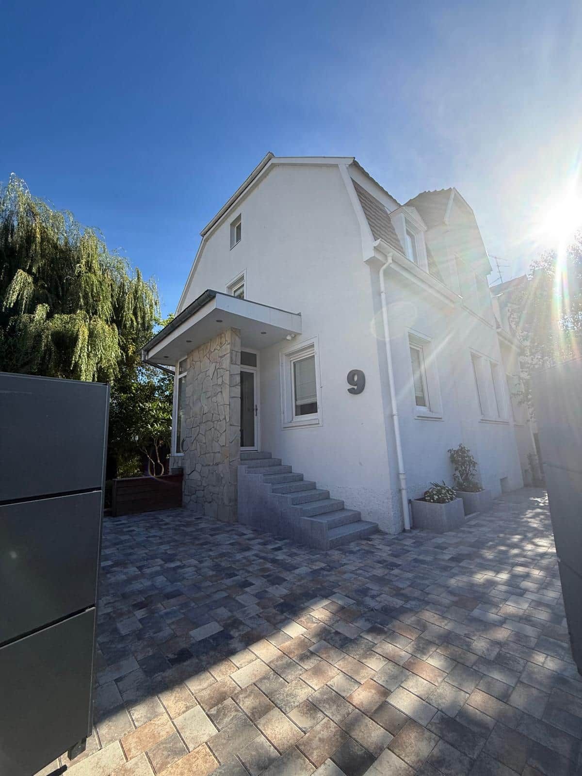 A two-story house with a stone facade, a number '9' on the front, and a paved driveway leading to the entrance.