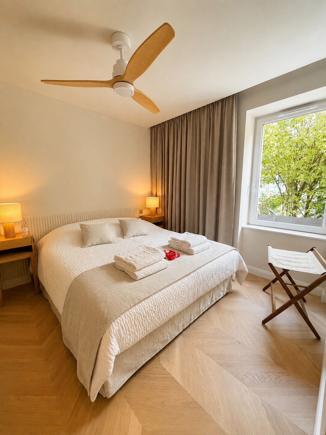 Une chambre d’hôtel avec un lit, un ventilateur de plafond, une fenêtre avec des rideaux et une table de chevet avec une lampe.