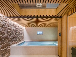 A spa area with a stone wall, wooden ceiling, and a hot tub.