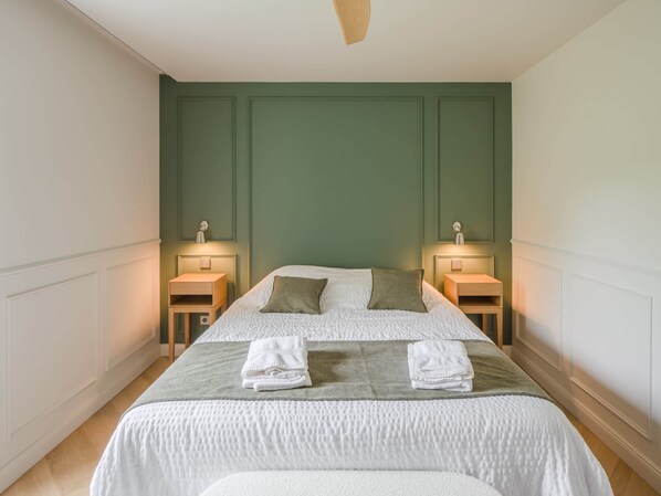 A neatly made bed with pillows and folded towels, two bedside tables with lamps, and a green wall paneling.