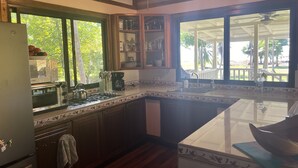 Une cuisine équipée d’un four à micro-ondes, d’une cuisinière et d’un évier. Une fenêtre offre une vue sur les arbres, et une terrasse se trouve à l’extérieur.
