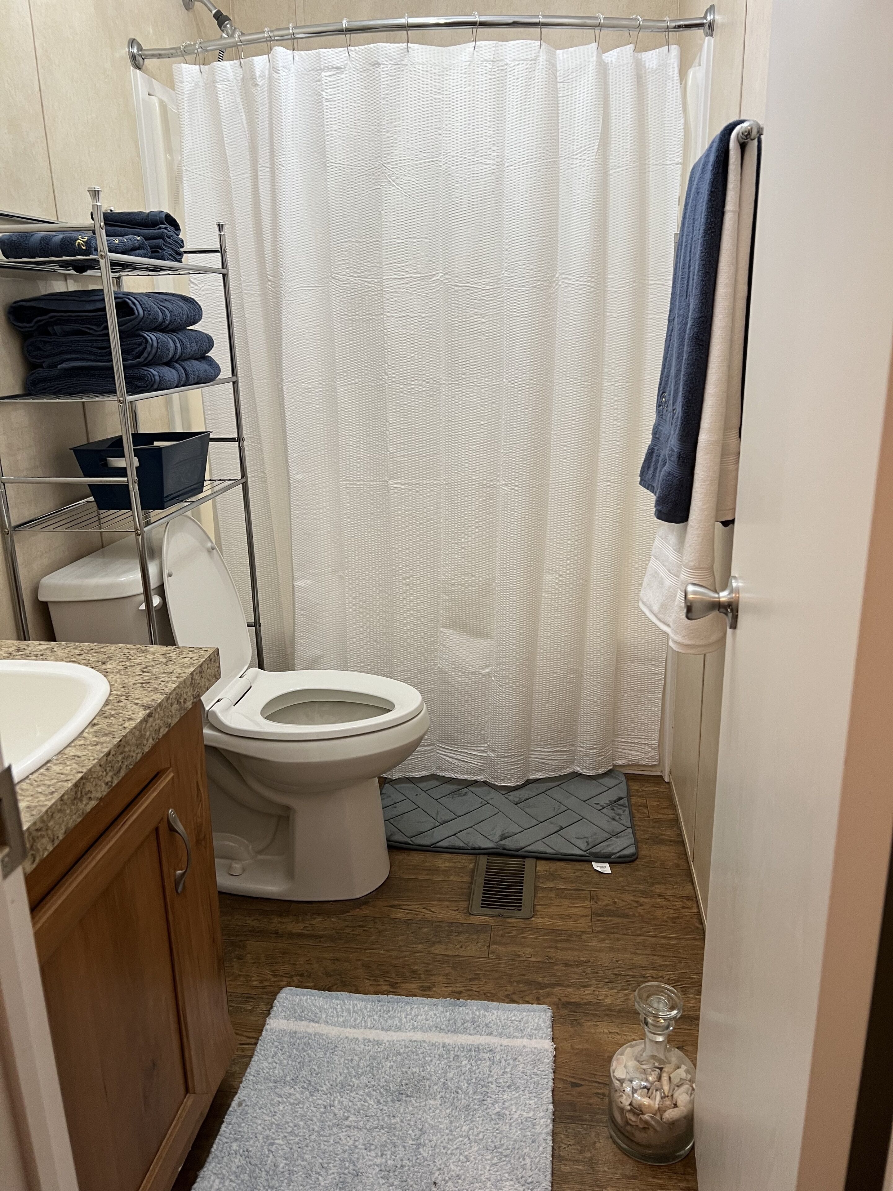 Een badkamer met toilet, wastafel, douchegordijn, handdoekrek en een plank met opgevouwen handdoeken.