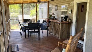 Un porche cubierto con una mesa y sillas de madera, una mecedora y una zona de bar.