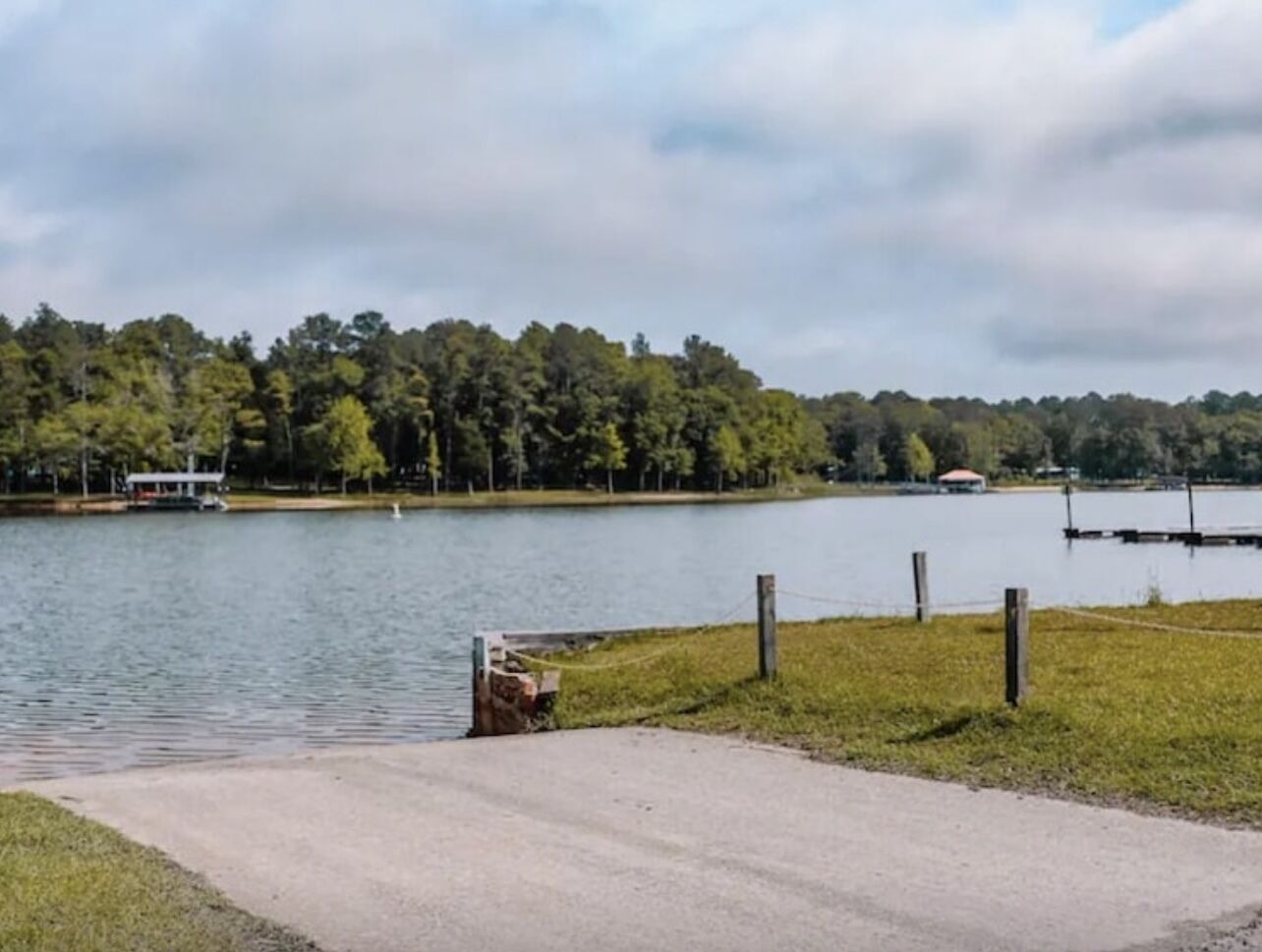 A lakeside view with a dock, grassy area, and a small building near the water.