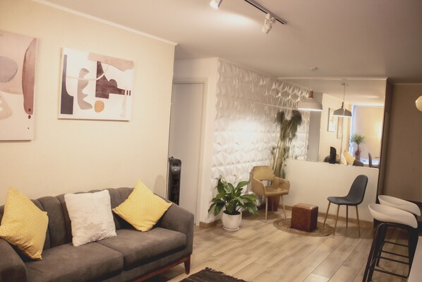 Un salon avec un canapé gris, des coussins jaunes et blancs, une plante en pot et des œuvres d’art abstraites accrochées au mur.