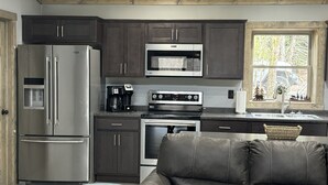 Cocina moderna con armarios oscuros, electrodomésticos de acero inoxidable, un sofá de cuero y una ventana con vistas a árboles.