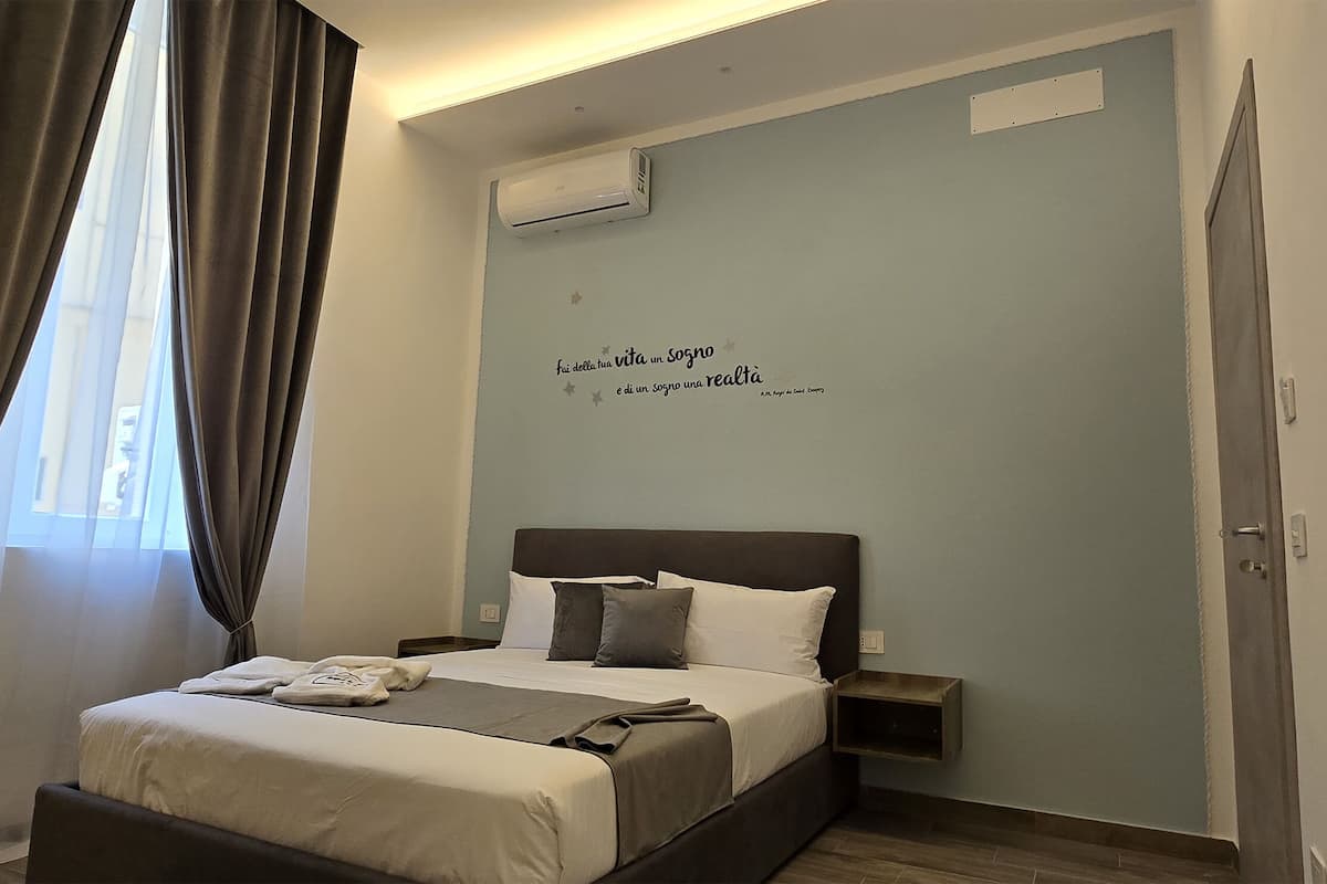 A neatly arranged hotel room with a bed, bedside tables, and an air conditioning unit on the wall.