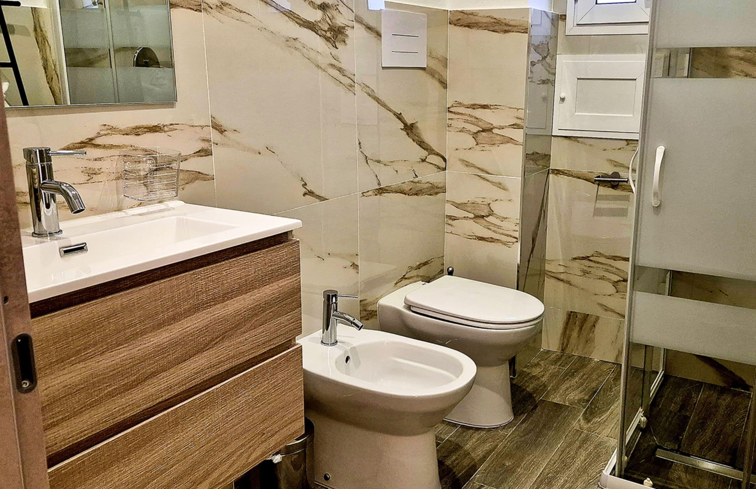 Un baño con pared de mármol, lavabo, bidé y retrete.