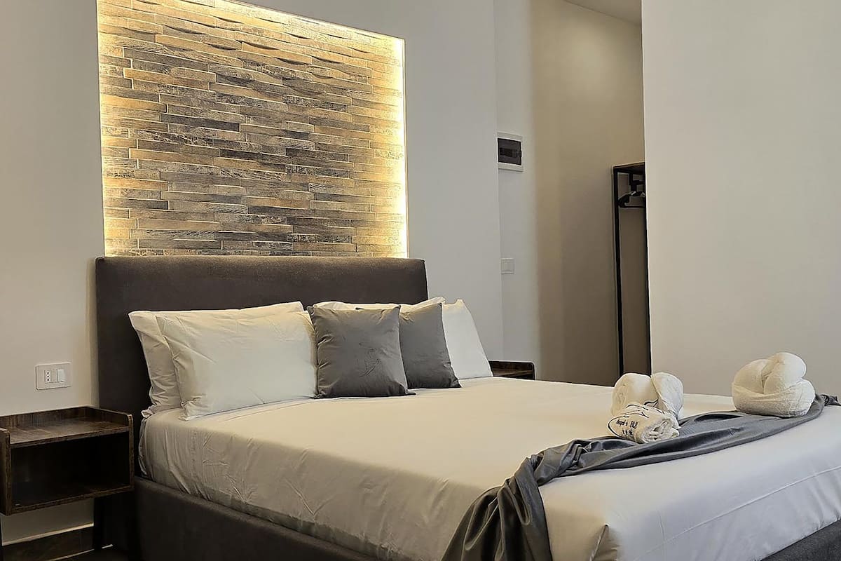 A modern hotel room with a large bed, a headboard with a textured wall, and a nightstand.