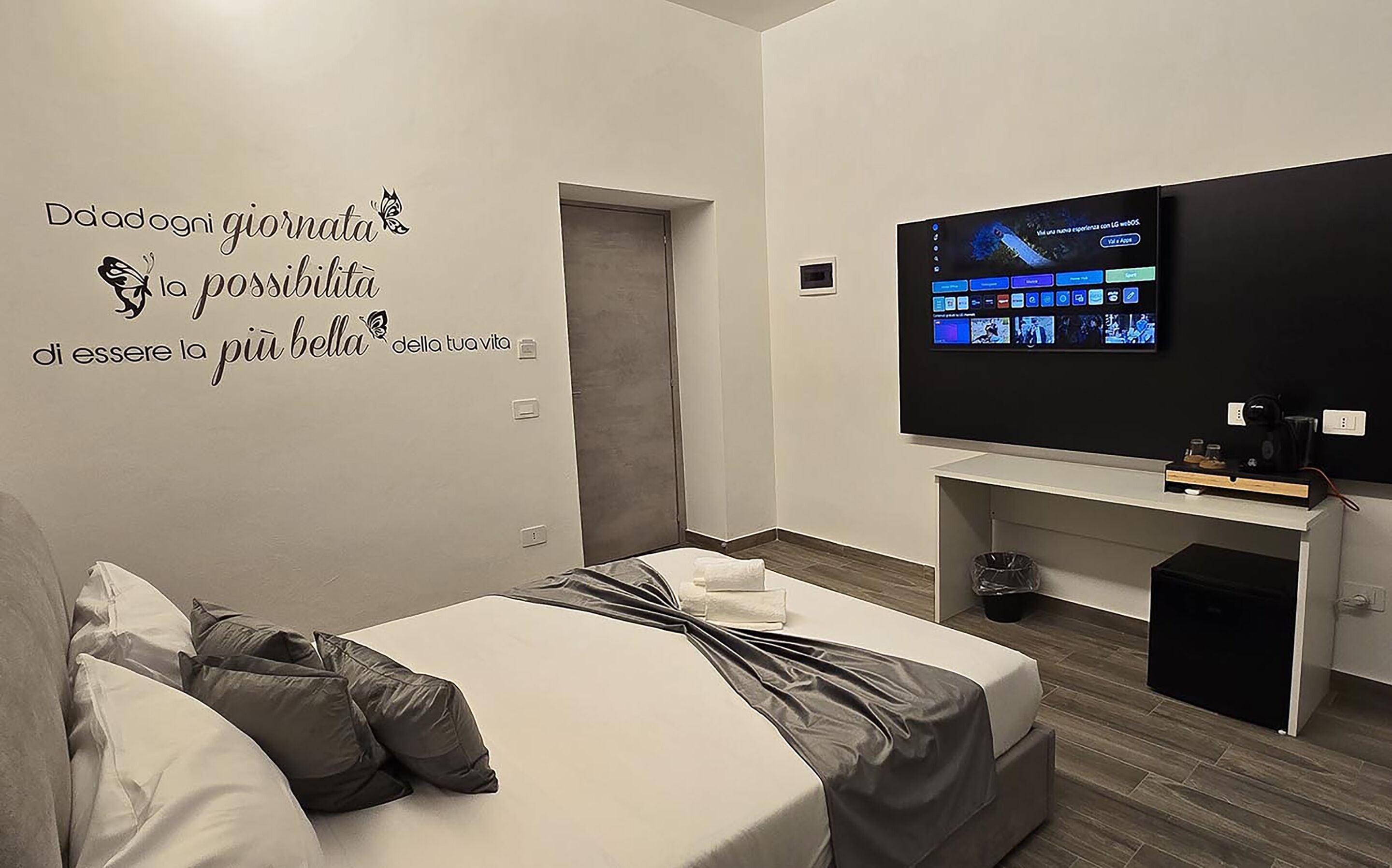 A modern hotel room with a bed, a desk, and a TV mounted on the wall.