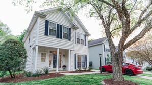 A two-story house with a front porch, a driveway, and a tree in the yard. - Claire's Charming Home near RDU and RTP (Raleigh)
