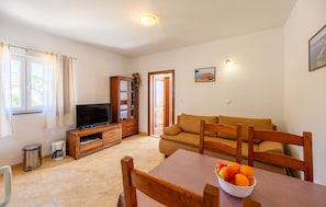 Un salón con sofá, televisor, aparador de madera y una mesa con fruta.