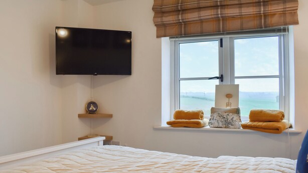 A bedroom with a bed, a TV mounted on the wall, a window with a view, and a bedside table with a lamp. - 3 bedroom accommodation in Easington, near Staithes (Easington, near Staithes)