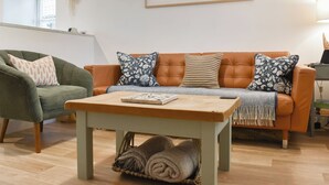 A living room with a green armchair, an orange sofa with patterned cushions, a wooden coffee table, and a framed landscape painting. - 3 bedroom accommodation in Easington, near Staithes (Easington, near Staithes)