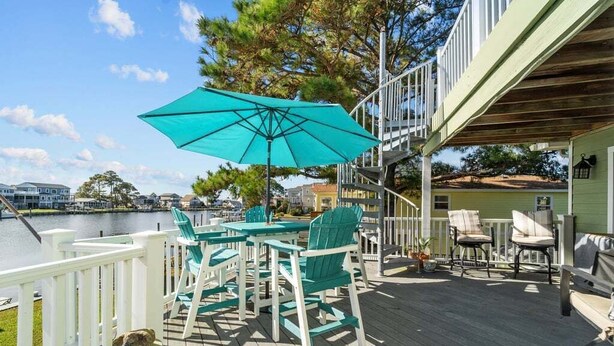 A deck with outdoor furniture, a turquoise umbrella, and a view of the water. - Garber Harbor in Colington Harbor Waterfront Canal  Hot Tub Jimmy Buffett Bar  (Kill Devil Hills)
