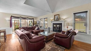 A living room with a sectional sofa, a fireplace, and a large window with blinds. - Garber Harbor in Colington Harbor Waterfront Canal  Hot Tub Jimmy Buffett Bar  (Kill Devil Hills)