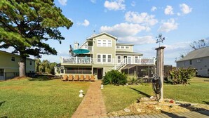 A two-story house with a front deck, a covered patio, and a small garden area. - Garber Harbor in Colington Harbor Waterfront Canal  Hot Tub Jimmy Buffett Bar  (Kill Devil Hills)