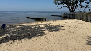 A sandy beach with a large tree, a wooden dock, and a white fence. - Garber Harbor in Colington Harbor Waterfront Canal  Hot Tub Jimmy Buffett Bar  (Kill Devil Hills)