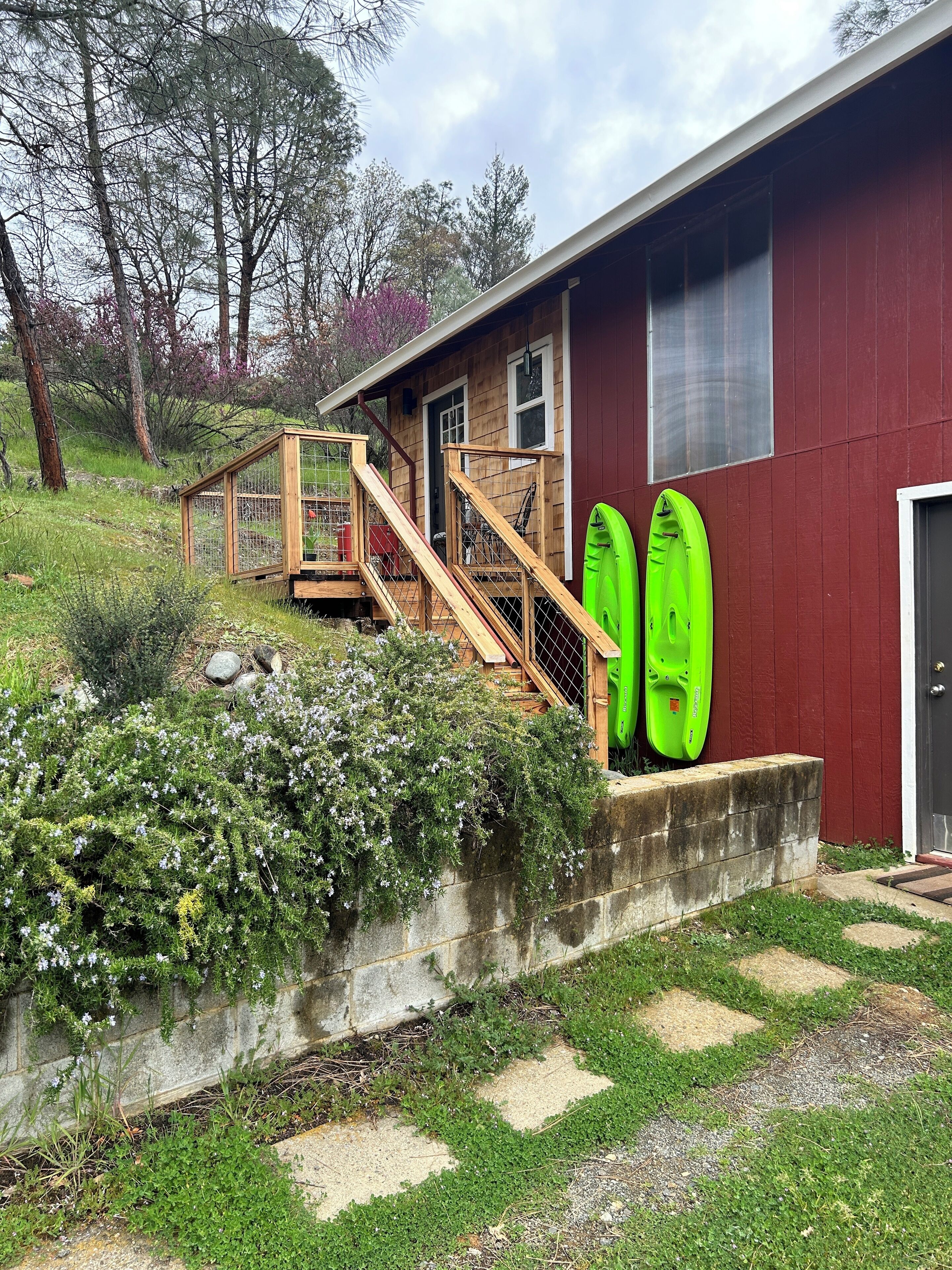 Une maison avec une terrasse en bois, un kayak vert et un mur en pierre.