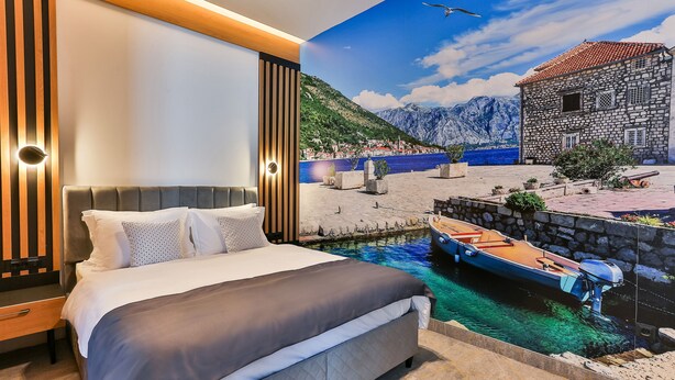 A bedroom with a bed, a nightstand, and a wall mural of a coastal scene with a boat and mountains. - Hotel Boka (Radanovici)