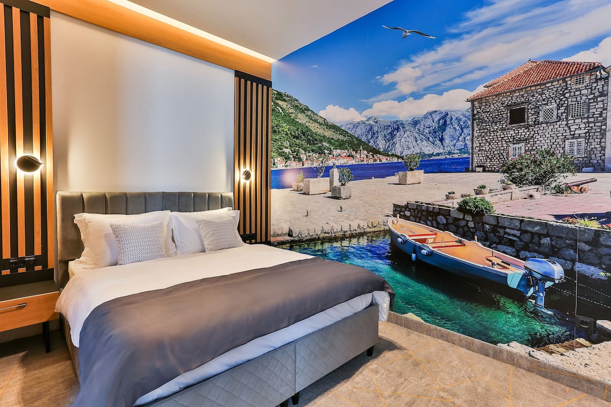 A bedroom with a bed, a nightstand, and a wall mural of a coastal scene with a boat and mountains.