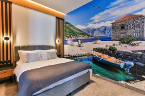 Un dormitorio con cama, mesita de noche y un mural en la pared que muestra una escena costera con un barco y montañas.