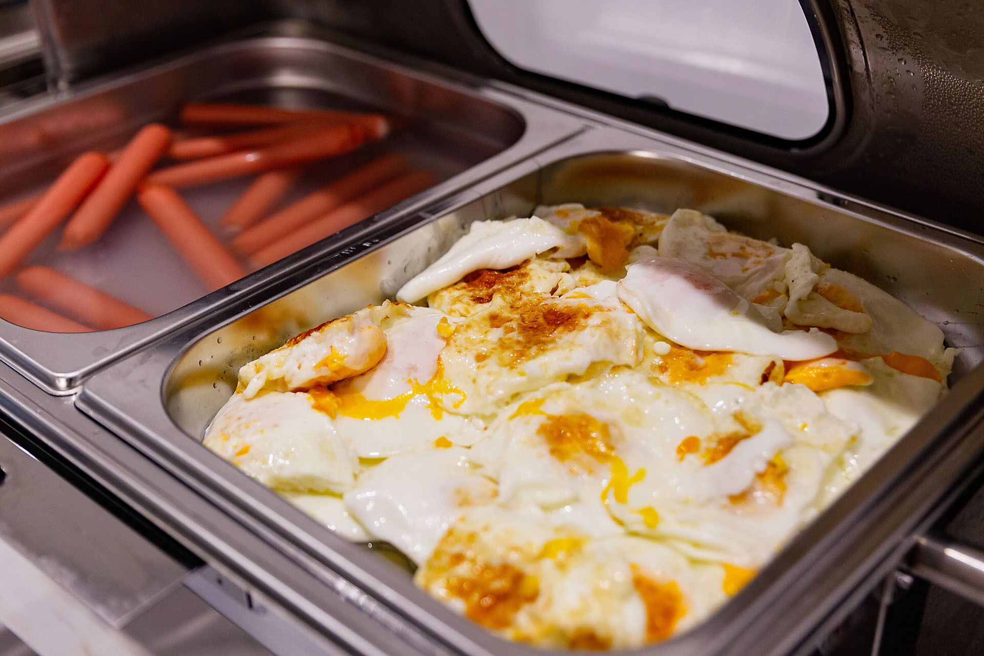 A buffet with a tray of eggs and a container of sausages.